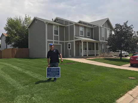 Denver area home with man standing out front holding a Diamond Exteriors Roofing sign